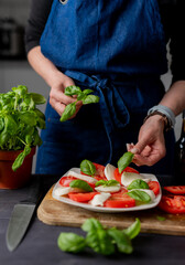 Woman Decorates Caprese Salad With Basil, Made From Tomatoes And Mozzarella Cheese