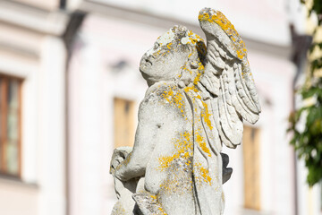 Plague column detail - old statue of angel with blurred historical buildings on background, Telc,...
