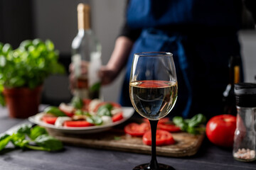 White Wine Glass On Blurred Background Of Woman And Caprese Salad, Close-Up Shot