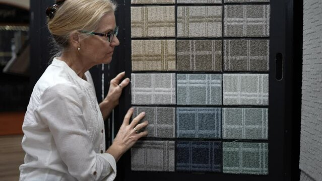 Smiling happy mature woman turning page of carpet samples looking for home redecorating project, in a design center floor store.