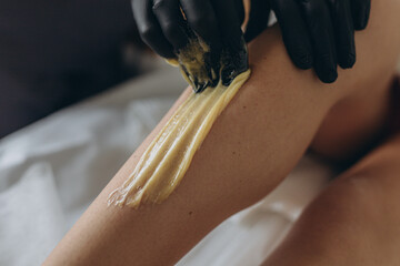 Beautician depilating young woman's legs with liquid sugar in spa center