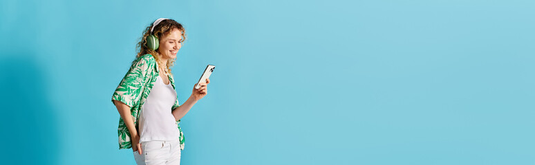 Curly-haired woman holding phone against vibrant blue backdrop.