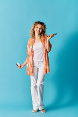 Curly-haired woman holding cell phone against blue background.