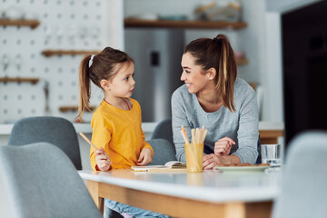 A happy mother and her daughter talking and drawing together at home