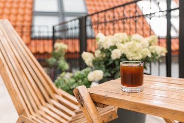 A glass of iced coffee on a wooden table next to a wooden chaise longue on the terrace.