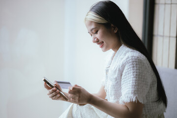 Attractive millennia Asian female holding her smartphone and credit card, using mobile banking app...