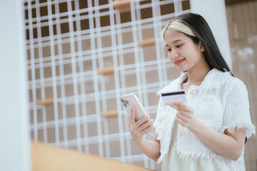 Attractive millennia Asian female holding her smartphone and credit card, using mobile banking app...