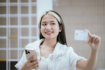 Attractive millennia Asian female holding her smartphone and credit card, using mobile banking app...