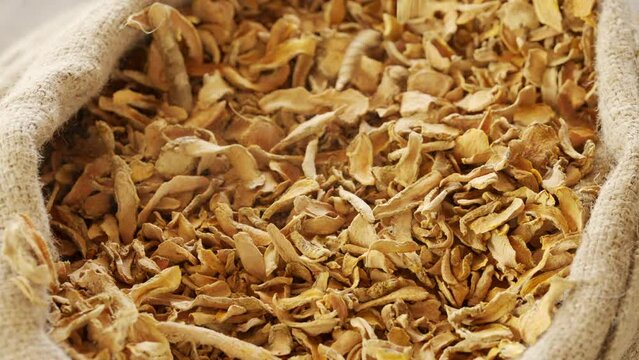 Sliced dried turmeric spice falling in slow motion in burlap sack, curcuma longa root, harvest