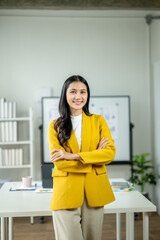 A woman in a yellow jacket stands in front of a white board with a smile on her