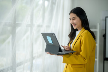 A woman in a yellow jacket is smiling while using a laptop