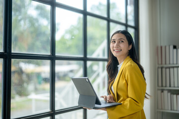 A woman in a yellow jacket is holding a laptop in front of a window