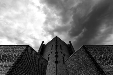 Brick facade of Peace Church of Königsmünster Abbey in Meschede in Sauerland (Germany) from a worm's eye view from below with dramatic cloud formations in the sky. Church building and monastery.