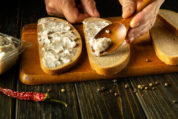 Making sandwiches on the kitchen table from fat and bread for a snack. A spoon in the hands of a...