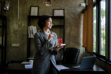 A woman in a gray suit is sitting at a desk with a laptop and a notebook