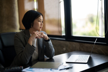 A woman in a business suit sits at a desk with a laptop open