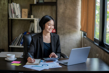 A woman is sitting at a desk with a laptop and a calculator