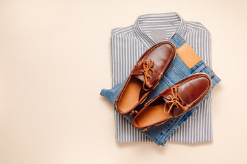 Men's casual outfit set top view with copy space. Male shirt with jeans and leather moccasins shoes on beige background, fashionable look for spring and summer season