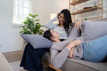 Fototapeta premium Asian lesbian couple relaxing on sofa at home. Concept of love and LGBTQ