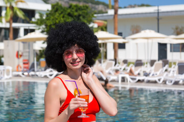 A girl enjoys the warm rays sun while drinking a drink near the pool.