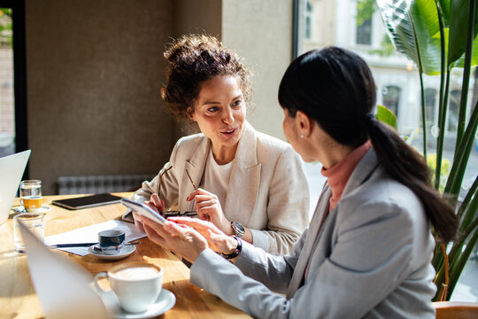 Two professional women discussing work at a cafe table