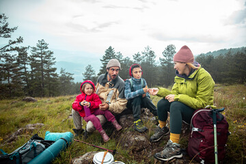 Family of four enjoying snacks during mountain hike in cloudy weather