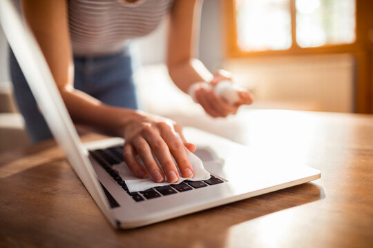 Woman disinfecting laptop keyboard with cleaning wipe