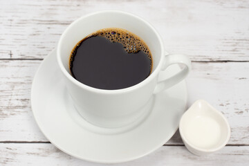 白い木目テーブルの上に置かれたコーヒーカップとコーヒーフレッシュ