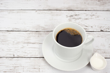白い木目テーブルの上に置かれたコーヒーカップとコーヒーフレッシュ