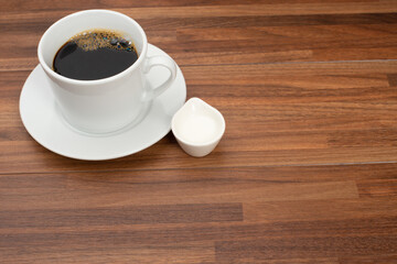 木目テーブルの上に置かれたコーヒーカップとコーヒーフレッシュ