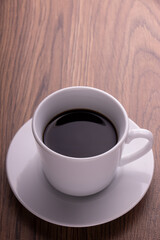 木目テーブルの上に置かれた白いカップのブラックコーヒー