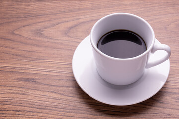 木目テーブルの上に置かれた白いカップのブラックコーヒー