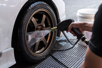 Cleaning and removing soap from the rim and tire of a car with a high pressure water spray gun. At a carwash shop.
