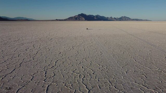 Back aerial view of chasing truck driving on Bonneville salt flats at golden hour in Utah
