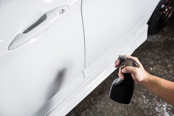 Spraying iron fallout remover on the side skirt or door of a car at a carwash.