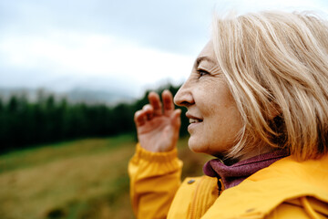 Close up portrait of a senior woman hiker looking away. Woman wearing yellow jacket standing on a...
