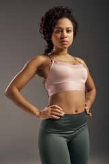 Curly African American sportswoman in pink sports bra and green leggings working out in studio with...