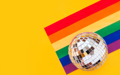LGBT rainbow flag and disco ball flat lay on yellow color background. gay marriage, human rights, june parade, lgbtq proud history month concept, coming out day. top view, place for text or logo