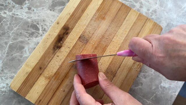 Top view of hand slicing sucuk sausage on cutting board