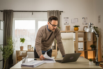 Adult businessman stand at office look on laptop and hold document