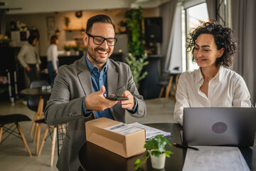 Colleagues sit at cafe scan packets with mobile phone check shipment