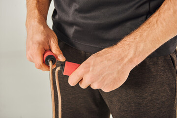 A young sportsman in active wear pulls a skipping rope with determination in a studio against a grey background.