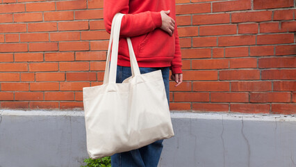 Woman in red hoodie holding tote canvas blank eco bag on street brick wall background. Female...