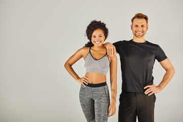 A young man and woman in sportswear strike a fashionable pose together against a grey studio backdrop.