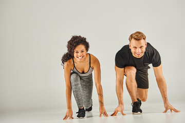 Young interracial sport couple in active wear pushing up together on gray background, showcasing...