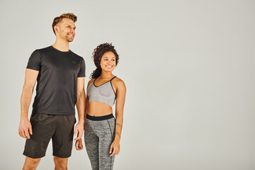 A man and a woman, both in active wear, standing side by side against a grey background in a studio setting.