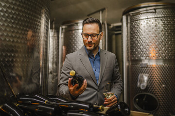 Adult man stand sommelier in basement and hold bottle wine