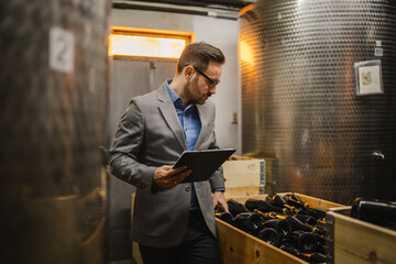 Adult man stand sommelier in basement look wine and hold clipboard