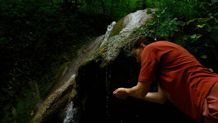 Young woman drinking water from cascade waterfall at deep tropical rain forest. Creative. Female...