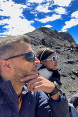 A man and woman are sitting on a rocky hillside, both wearing sunglasses